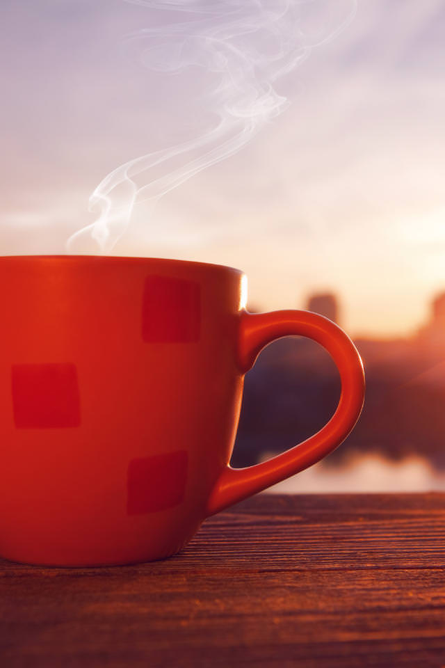 Dampfende Kaffeetasse vor einer Skyline mit Sonnenuntergang